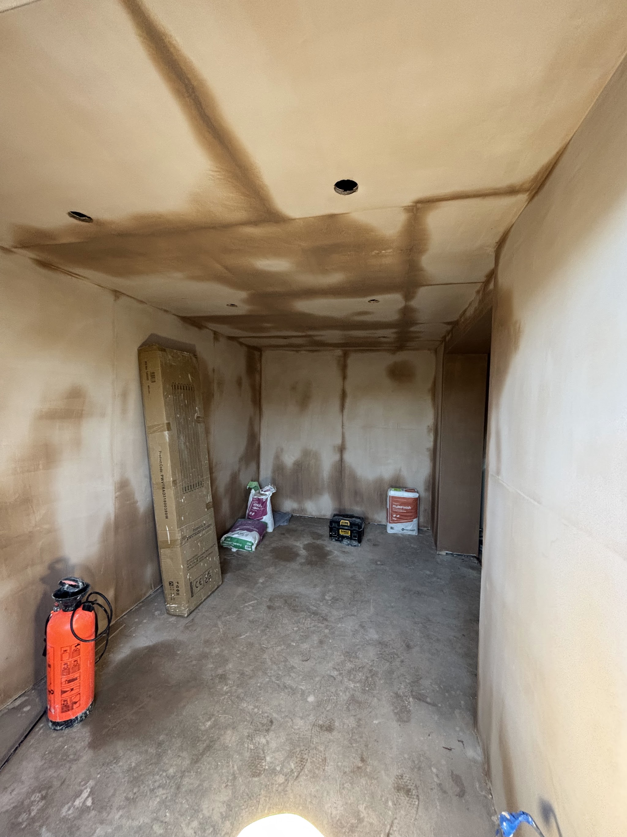 A room freshly skimmed by LRW Plastering, walls and ceiling drying out, with plaster bags and a sprayer on the floor