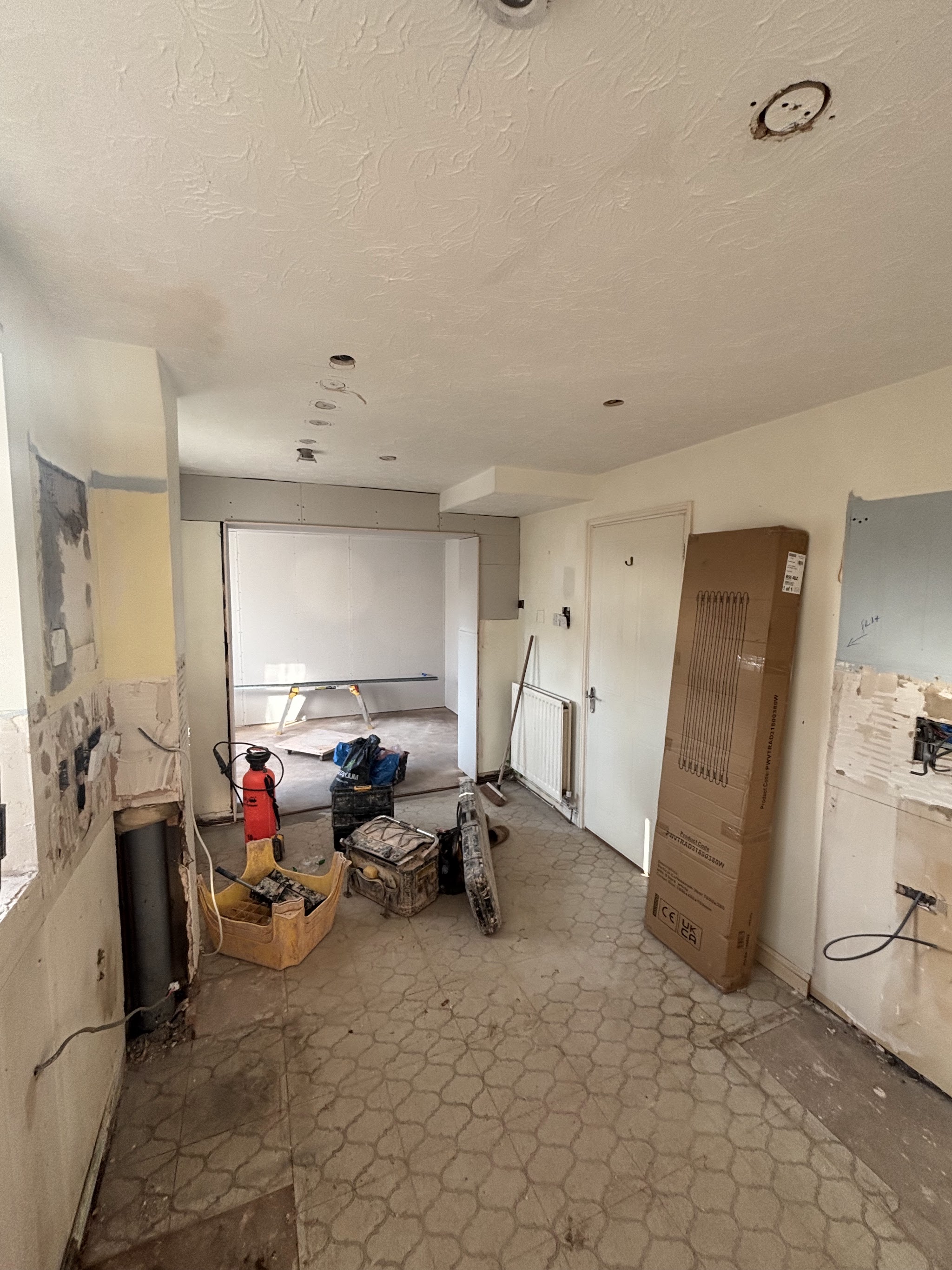 A room before plastering, with a textured ceiling and old floor tiles, tools set out