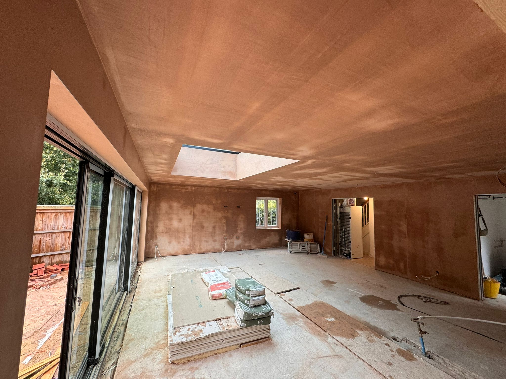 A large open extension with walls and ceiling freshly skimmed, a roof lantern and sliding doors