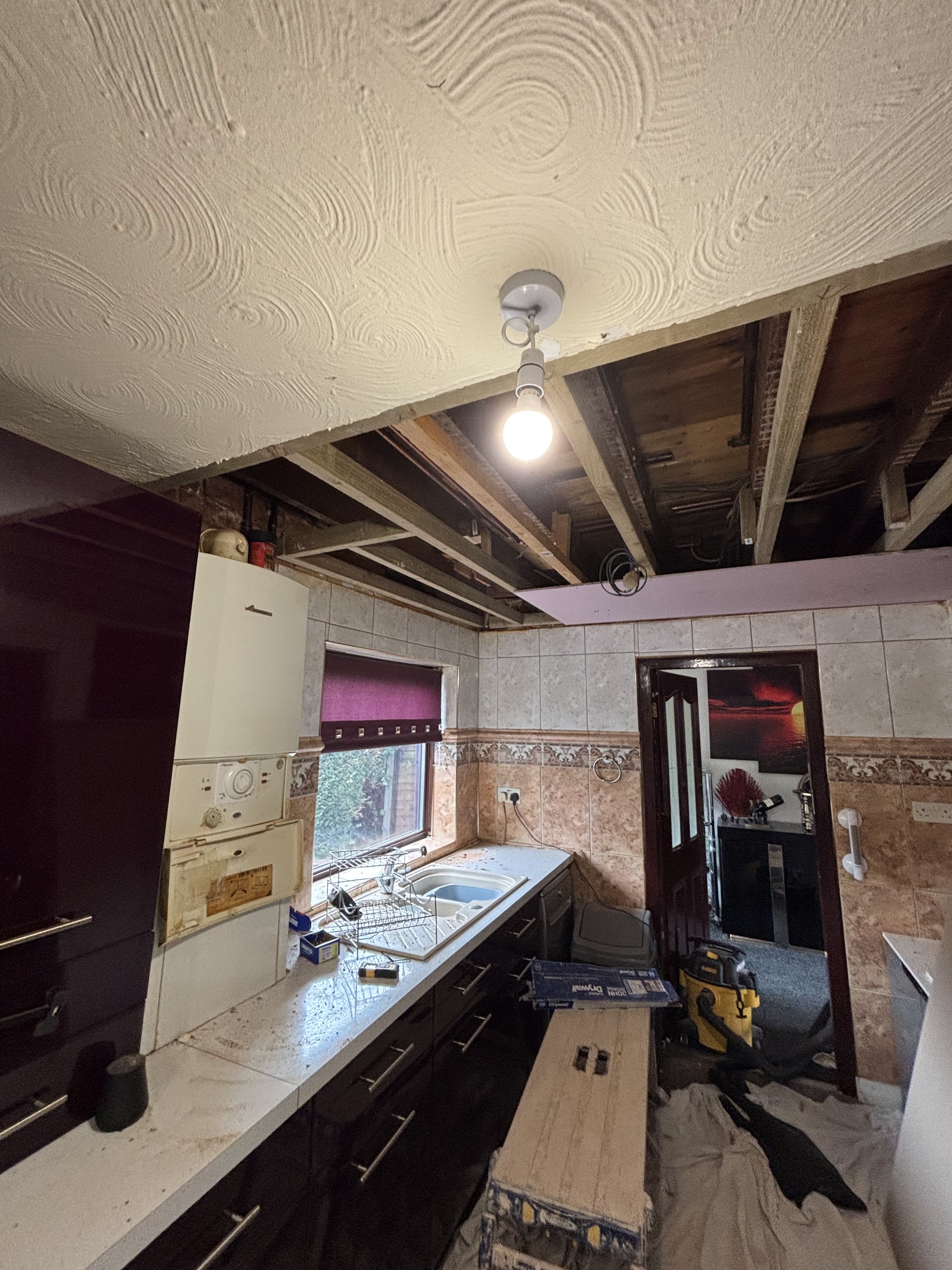 A kitchen with a swirl-textured ceiling partly taken down to the joists