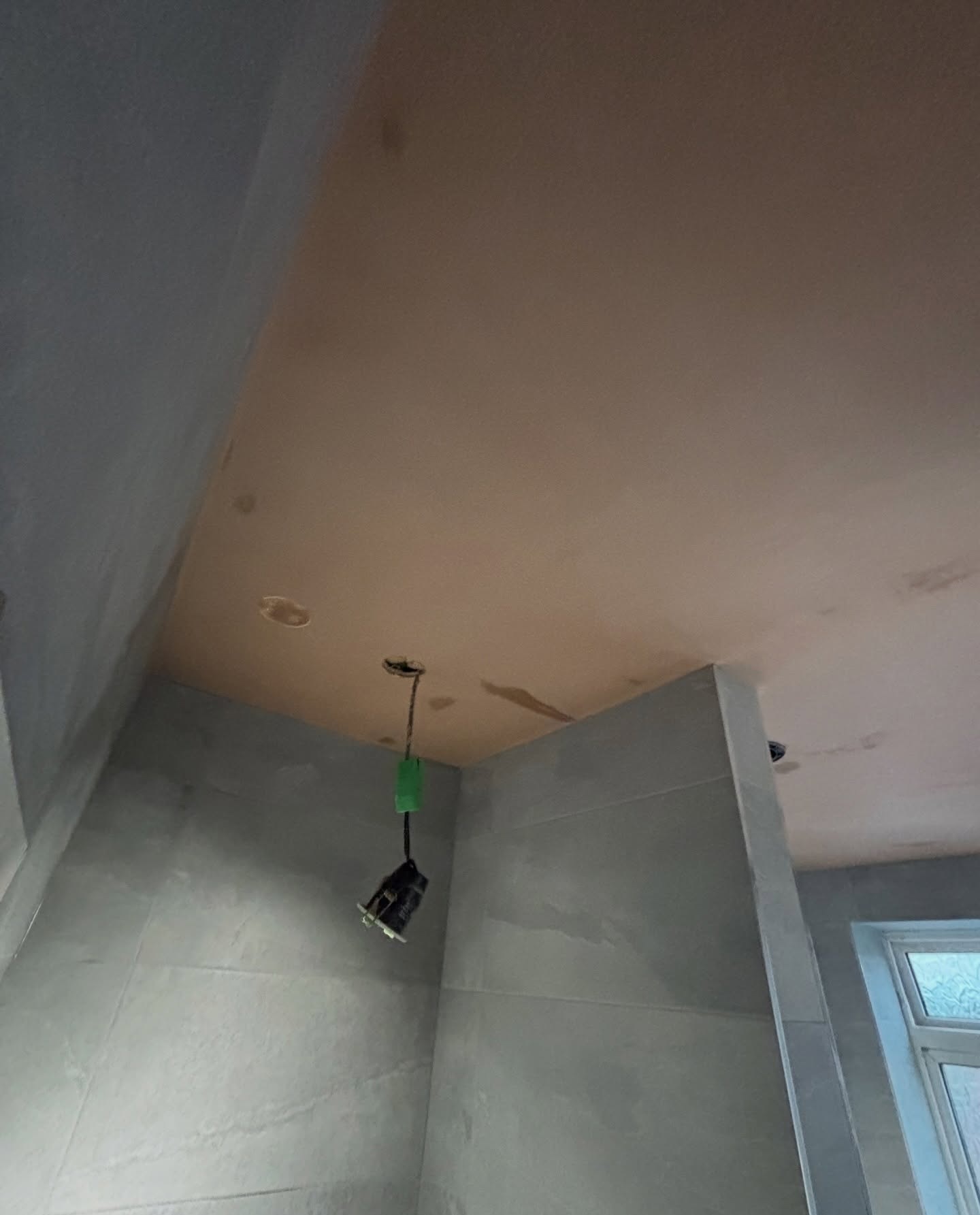 A bathroom ceiling freshly skimmed above newly tiled grey walls